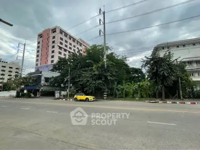 Street view of a modern pink building with lush greenery and a yellow car, perfect for urban living.