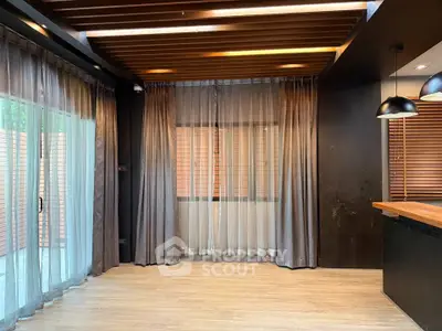 Modern living room with wooden flooring and stylish ceiling design, featuring large windows with elegant curtains.