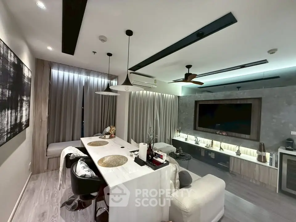 Modern living room with stylish decor, featuring a large TV, elegant lighting, and a cozy seating area.