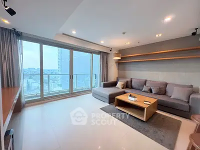 Spacious modern living room with large windows and city view, featuring a stylish gray sofa and wooden coffee table.
