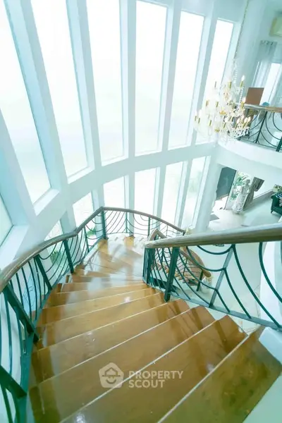 Luxurious staircase with elegant chandelier and floor-to-ceiling windows in a modern home.