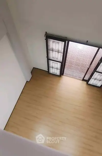 Spacious empty room with wooden flooring and large windows leading to a patio.