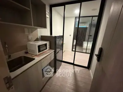 Modern compact kitchen with microwave and fridge, featuring sleek cabinetry and glass sliding doors.
