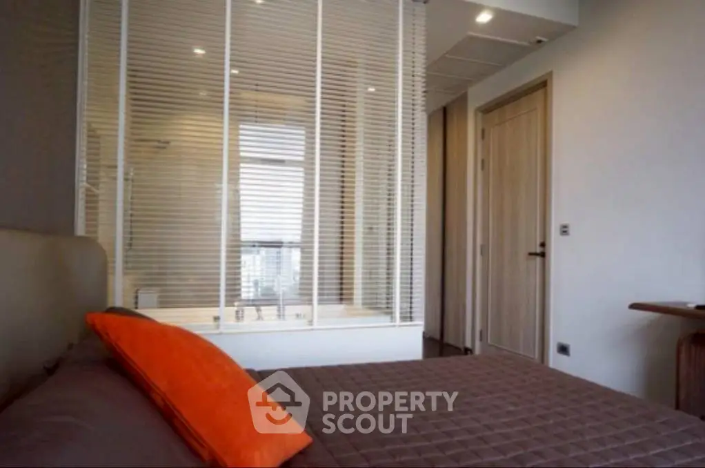Modern bedroom with a view into a stylish bathroom through glass partition.