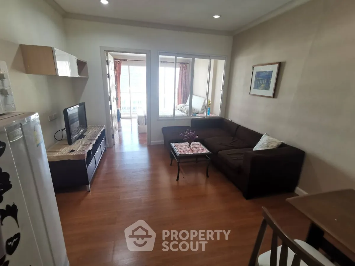 Cozy living room with wooden flooring and modern furniture, leading to a bright balcony with city views.