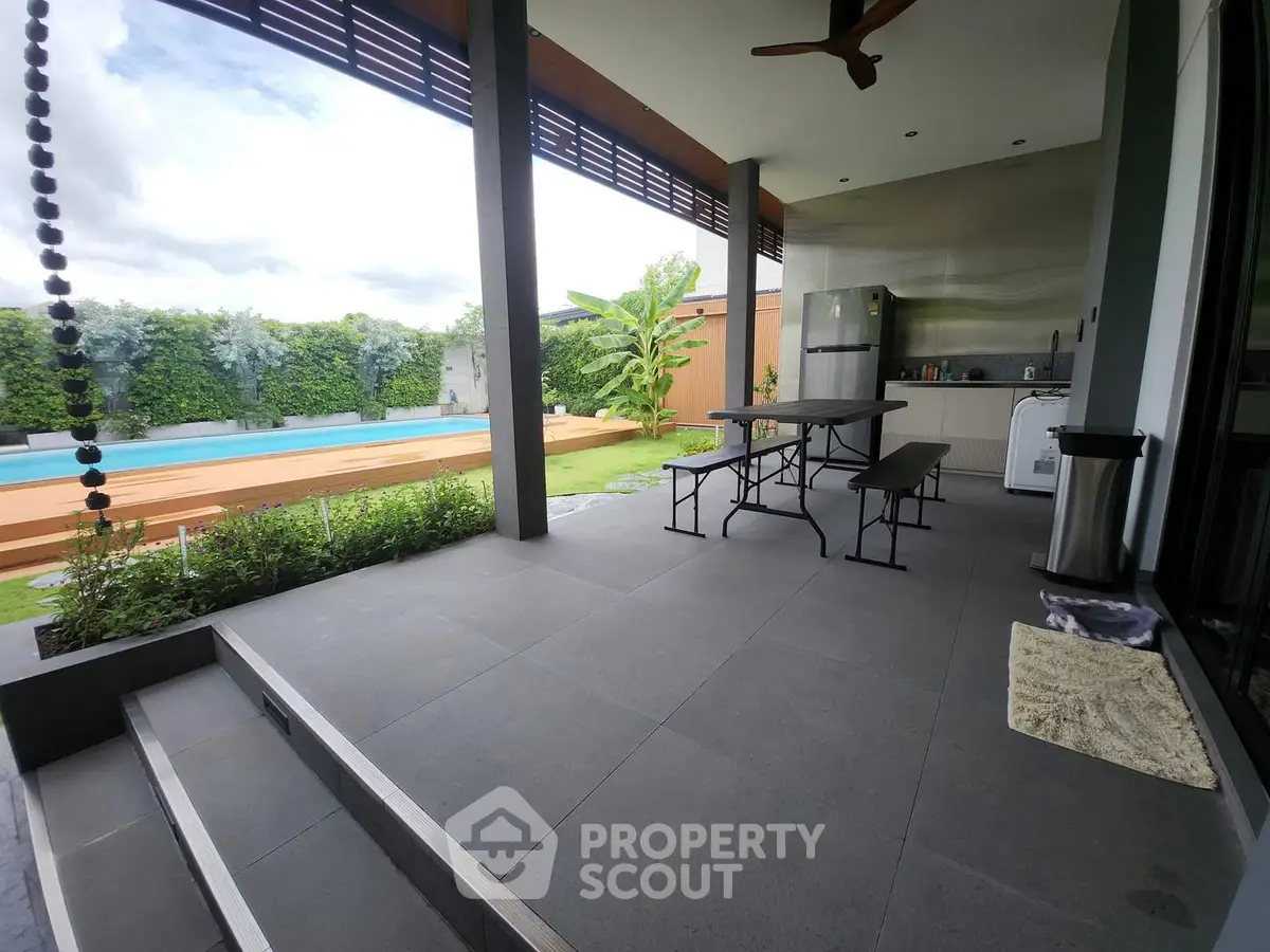 Modern outdoor patio with pool and garden view, featuring sleek design and stainless steel appliances.