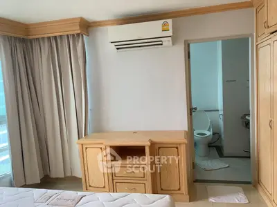 Cozy bedroom with ensuite bathroom and wooden furniture, featuring air conditioning and natural light.