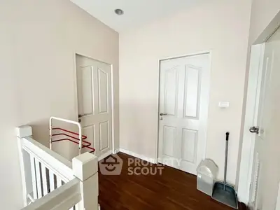 Bright hallway with wooden flooring and white doors, featuring a staircase and cleaning tools.