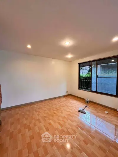 Spacious empty room with wooden flooring and large window, ideal for customization.