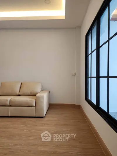 Modern living room with beige sofa and large window, featuring sleek wooden flooring.