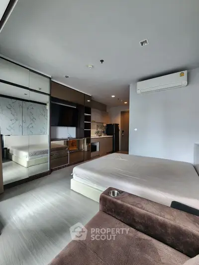Modern bedroom with sleek design, mirrored wardrobe, and compact kitchen area.