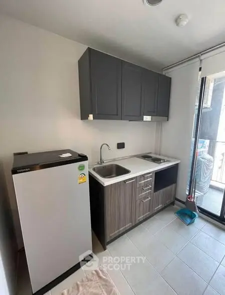 Modern compact kitchen with sleek cabinets and appliances, featuring a fridge and stovetop, ideal for urban living.