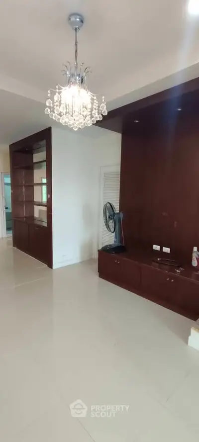 Spacious living room with elegant chandelier and built-in wooden shelving, perfect for modern living.