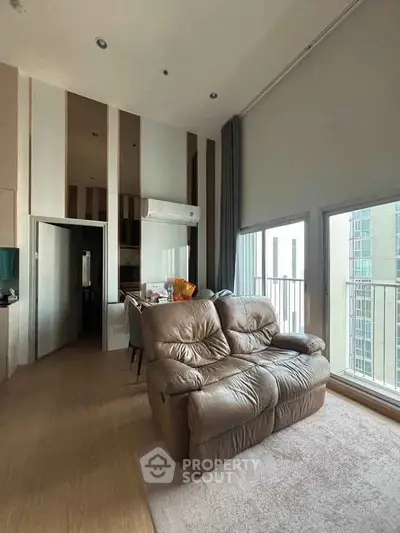 Spacious modern living room with high ceilings and large windows offering city views.