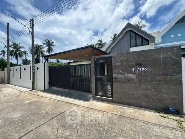 Modern house exterior with sleek gate and lush palm trees in tropical setting.