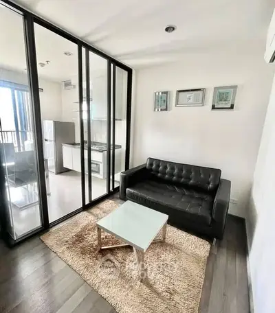 Modern living room with sleek black sofa and glass partition leading to kitchen.