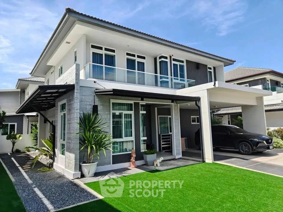 Modern two-story house with sleek design, large windows, and a spacious carport, surrounded by a well-maintained lawn.