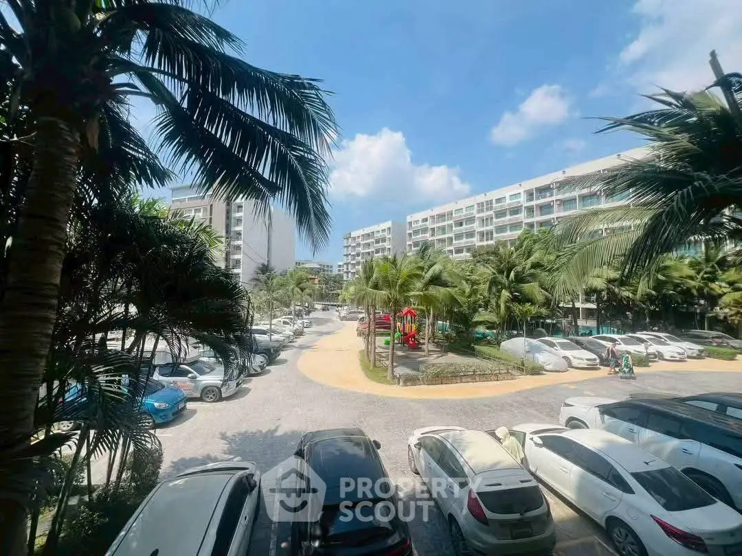 Spacious parking area surrounded by lush palm trees and modern apartment buildings under a clear blue sky.