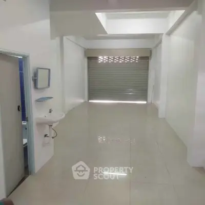 Spacious commercial space with tiled flooring and roll-up shutter, ideal for retail or office use.