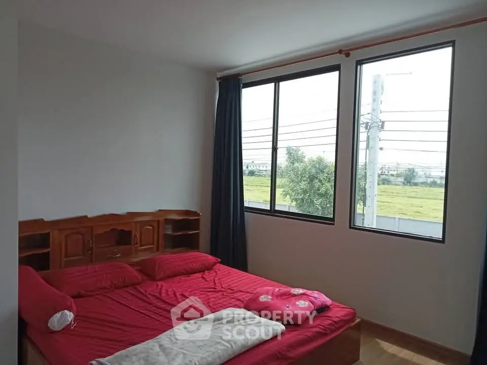 Cozy bedroom with large windows and red bedding, offering a serene view of greenery.