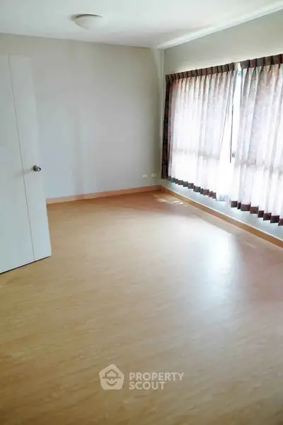 Spacious empty room with wooden flooring and large window, perfect for customization.