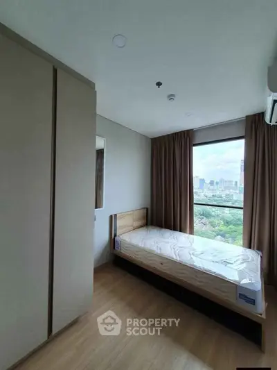 Cozy bedroom with city view, featuring a single bed and large window for natural light.