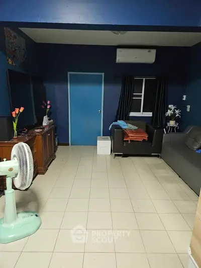 Cozy living room with blue walls, tiled floor, and air conditioning, featuring a fan and comfortable seating.
