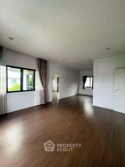 Spacious empty room with large windows and wooden flooring, perfect for customization.