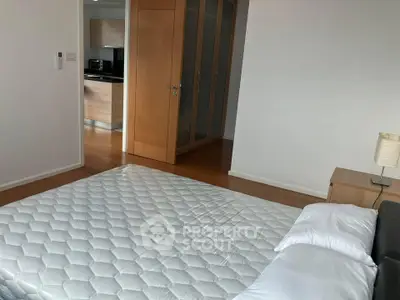 Spacious bedroom with modern design and wooden flooring, featuring a comfortable bed and a glimpse of the kitchen.