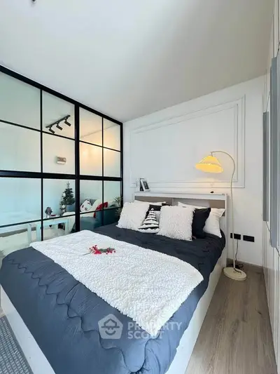Modern bedroom with stylish decor and glass partition, featuring cozy bedding and elegant lighting.