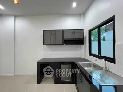 Modern kitchen with sleek black cabinetry and large window for natural light.