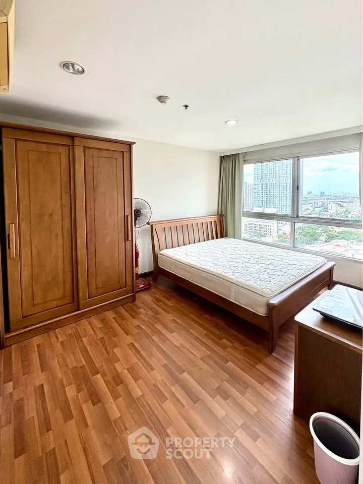 Spacious bedroom with wooden flooring and city view, featuring a large wardrobe and comfortable bed.
