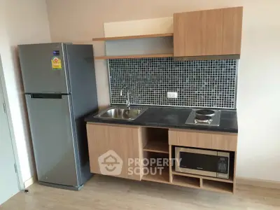 Modern compact kitchen with sleek cabinetry, stainless steel fridge, and built-in microwave in a stylish apartment.