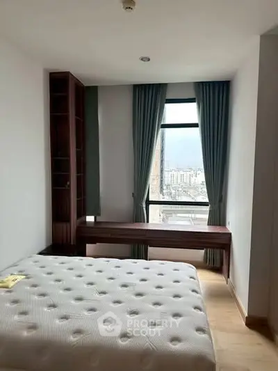 Bright bedroom with city view, featuring a large window, wooden desk, and comfortable bed.