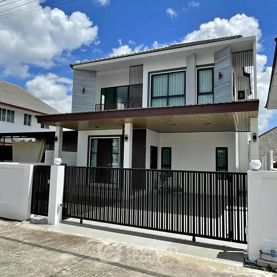 Modern two-story house with sleek design and gated entrance under a clear blue sky.