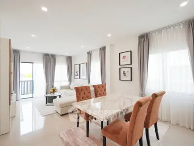 Elegant modern living room with dining area, featuring marble table and plush chairs, abundant natural light.