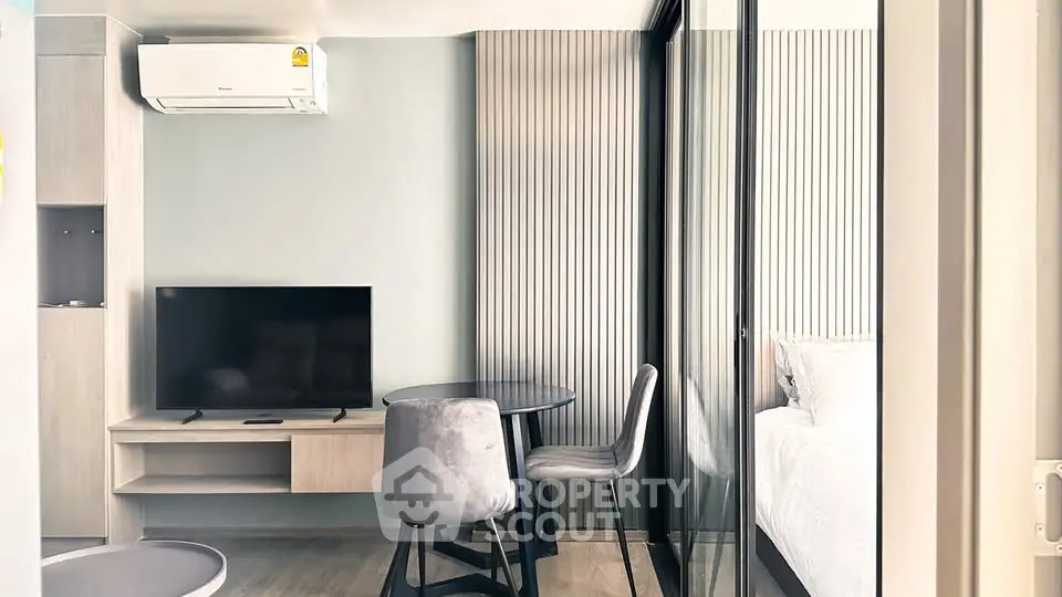 Modern compact living room with TV and air conditioning, adjacent to a cozy bedroom.