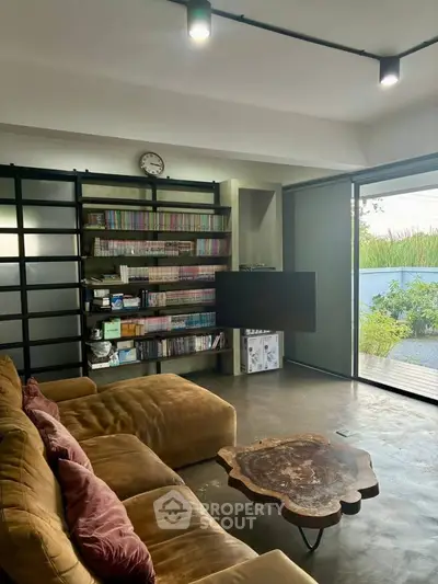 Stylish living room with cozy sofa, unique wooden table, and expansive bookshelf overlooking a serene garden view.