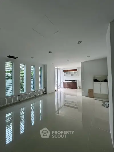 Spacious modern living room with glossy floors and large windows, leading to a sleek open kitchen.