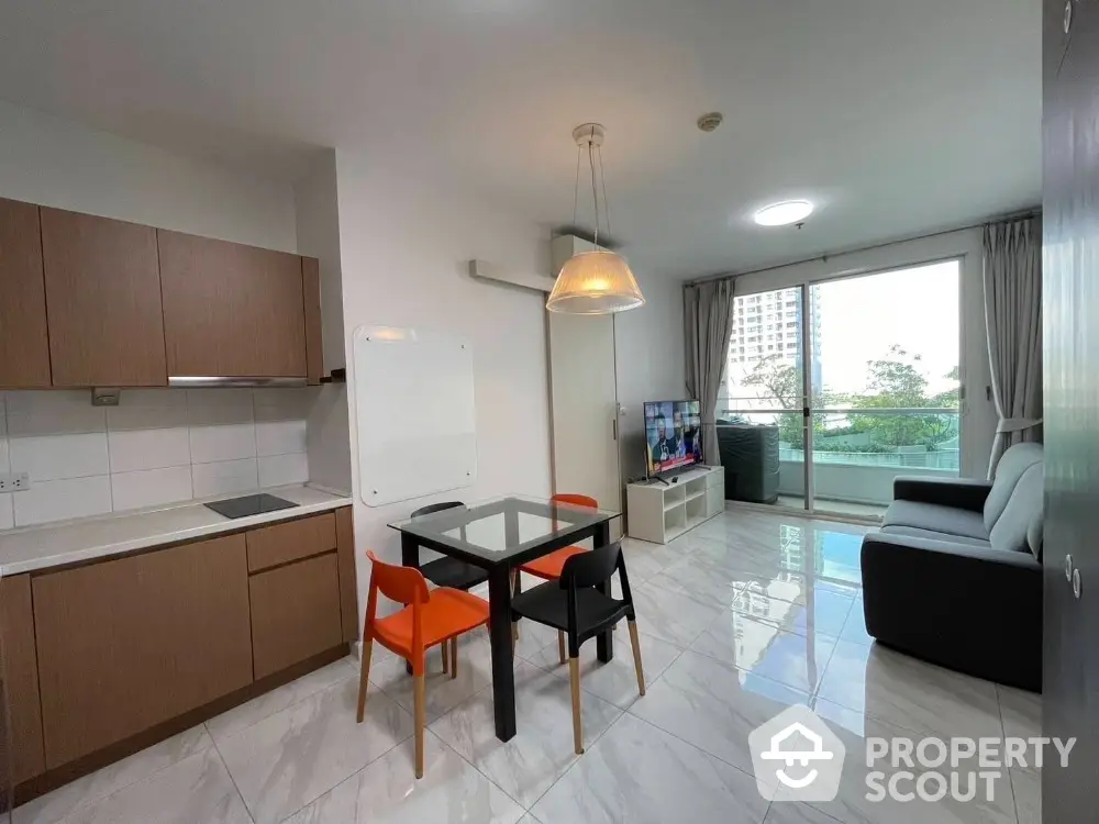 Modern open-layout living room with kitchen, featuring sleek furniture and large window with balcony view.