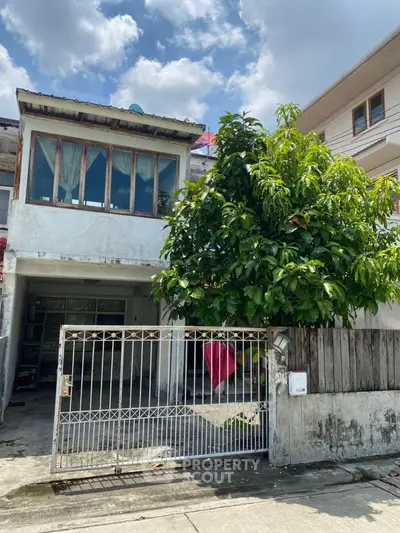 Charming two-story house with gated entrance and lush greenery in urban setting.
