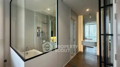 Modern apartment interior with glass-walled bathroom and city view, featuring sleek design and wooden flooring.