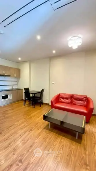Modern living room with red sofa, wooden flooring, and compact kitchen area.