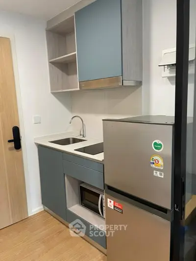 Modern compact kitchen with sleek cabinetry and stainless steel fridge in a cozy apartment.