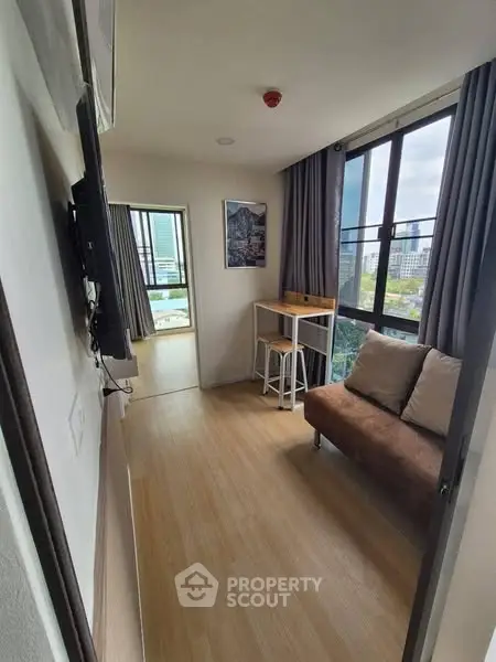 Modern apartment with cozy seating area and city view, featuring large windows and stylish decor.