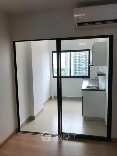 Modern kitchen with sliding glass doors and city view, featuring sleek cabinetry and air conditioning.