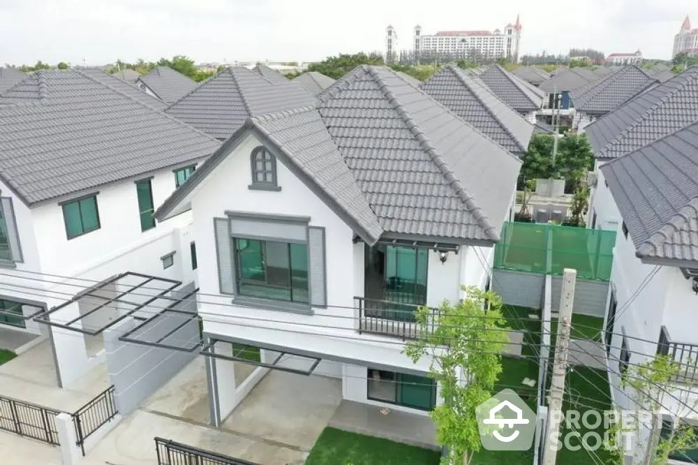 Aerial view of a modern suburban neighborhood showcasing stylish homes with dark tiled roofs, pristine white walls, and lush greenery, offering a serene and upscale living environment.