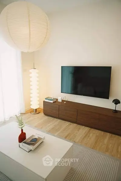 Modern living room with stylish decor and large TV, featuring a wooden floor and elegant lighting.