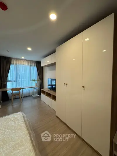 Modern bedroom with sleek wardrobe and cozy workspace near large window.