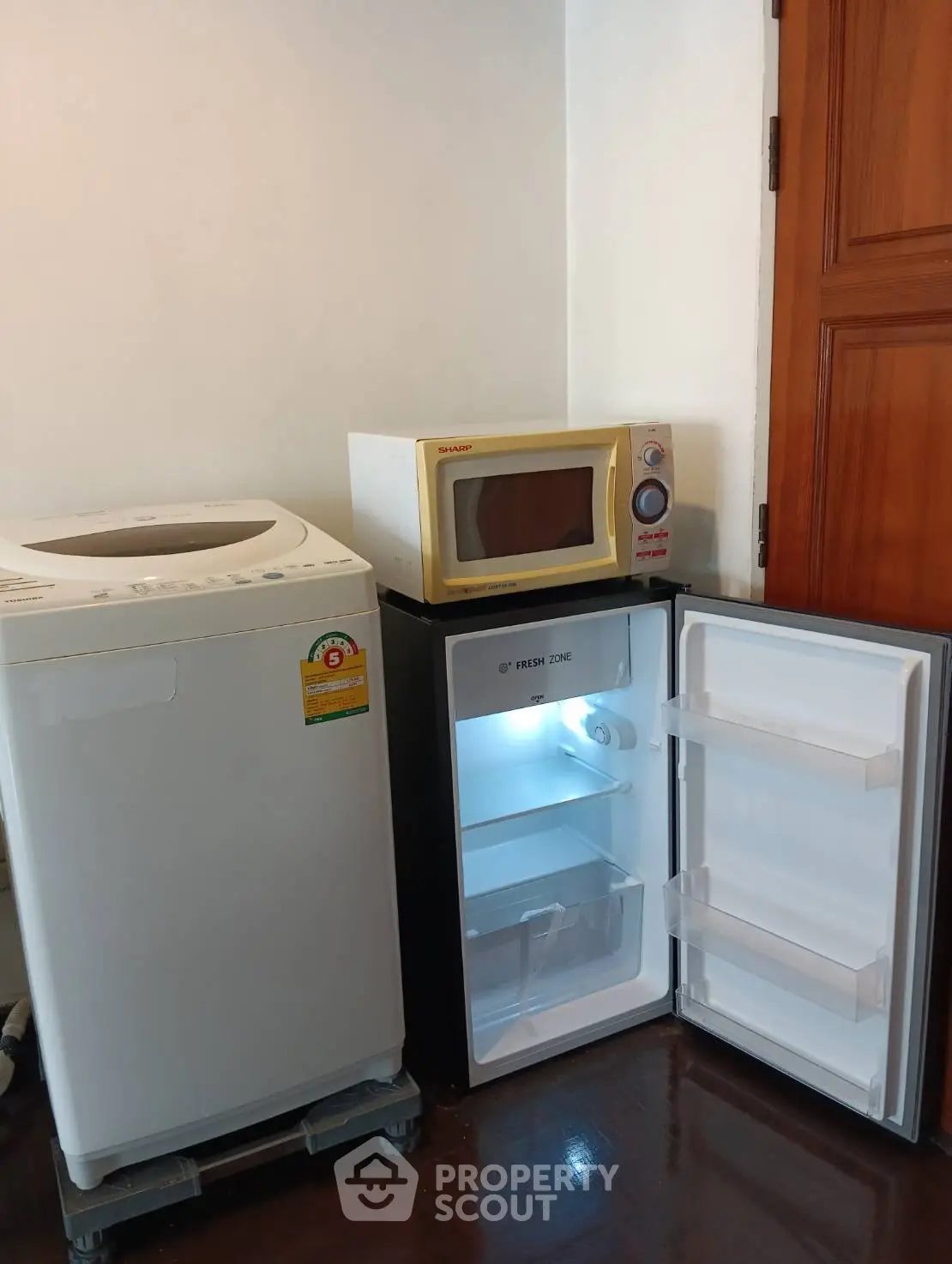 Compact laundry area with washing machine, fridge, and microwave in cozy home corner.